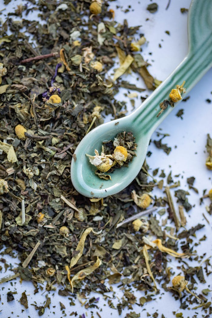 A detailed view of various dried herbs and flowers for herbal tea on a ceramic spoon.
