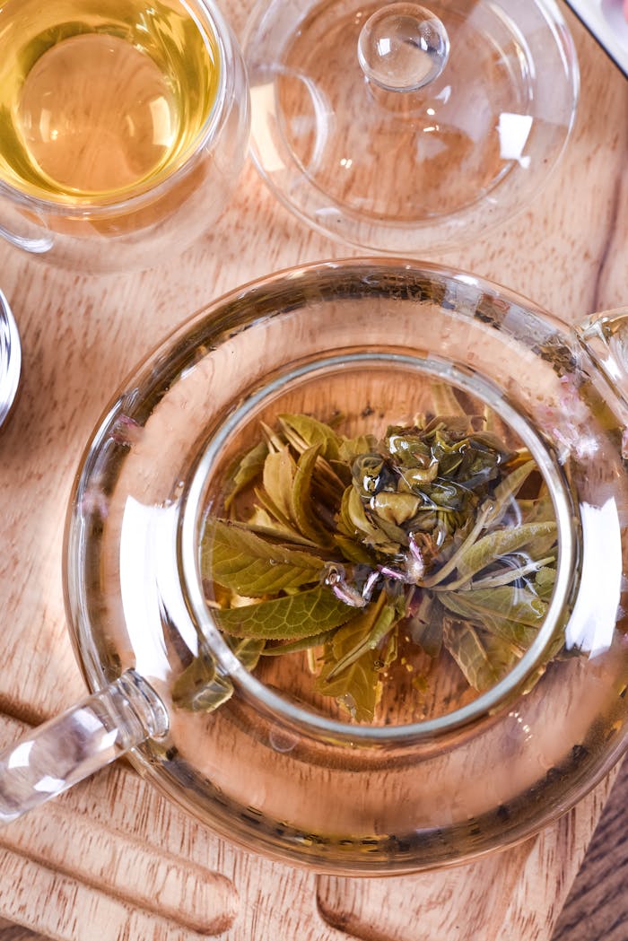 Overhead view of glass teapot with blooming herbal tea, creating a warm, inviting tea scene.